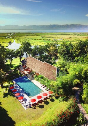 A pool area with a thatched-roof structure, surrounded by lush greenery and a clear view of distant mountains. - Villa Inle Boutique Resort (Nyaungshwe)