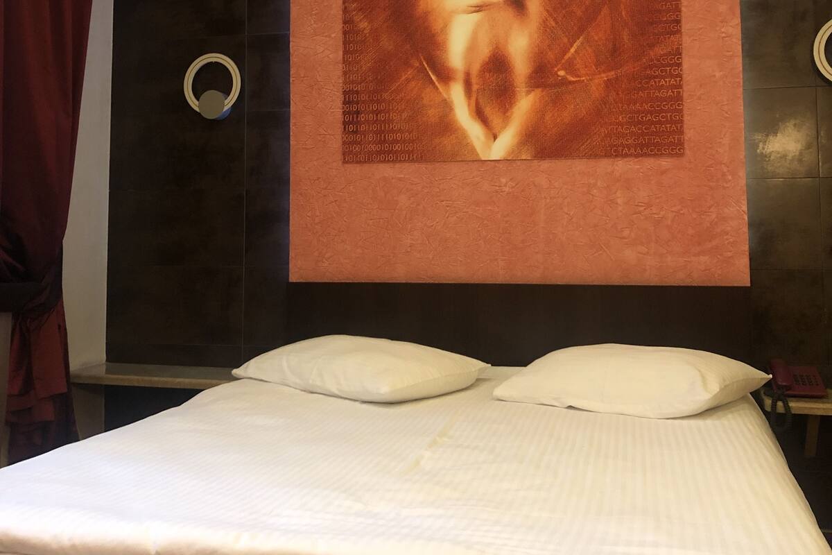 A modern hotel room with a large bed, a wall-mounted artwork, and a ring light fixture.