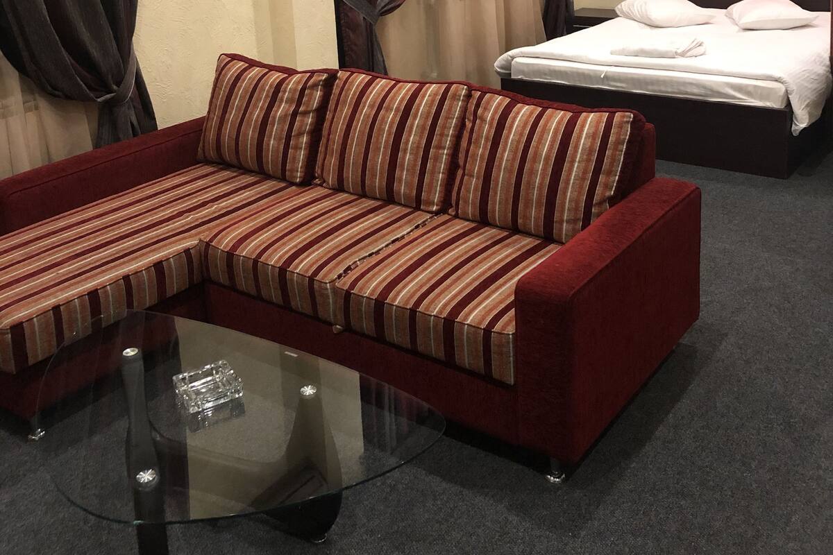A hotel room with a striped sofa, a glass coffee table, a bed with white bedding, and red and beige walls.