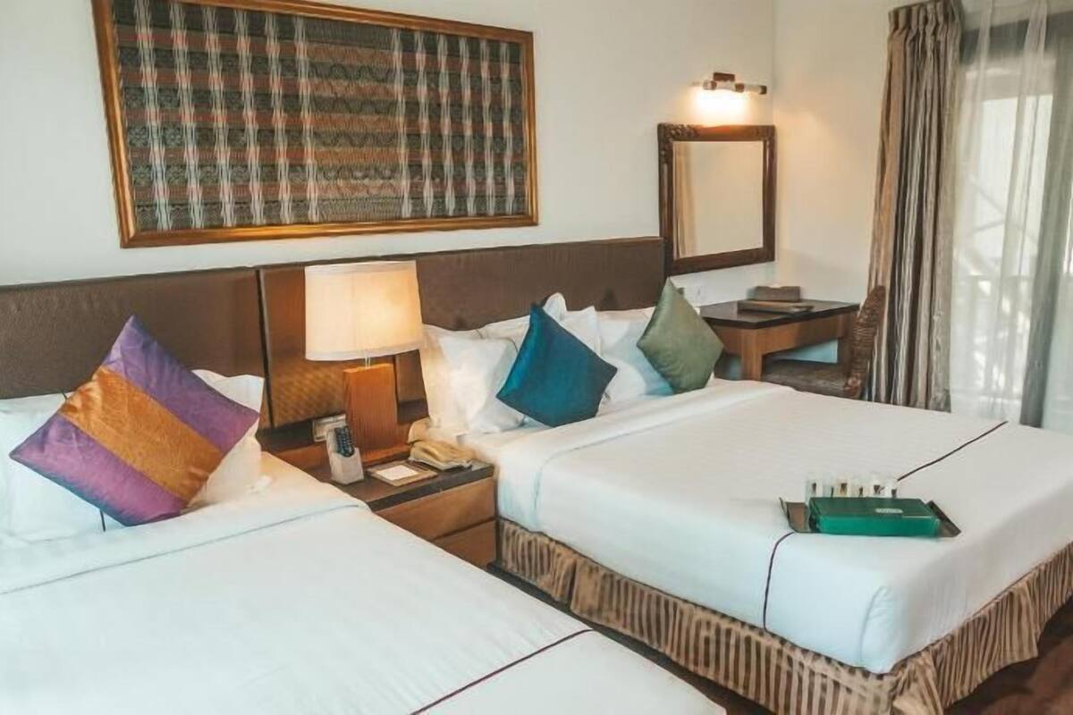A hotel room with two beds, a nightstand with a lamp, a mirror, and a table with a chair.