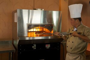 Un cocinero con uniforme opera un horno de leña para pizzas.