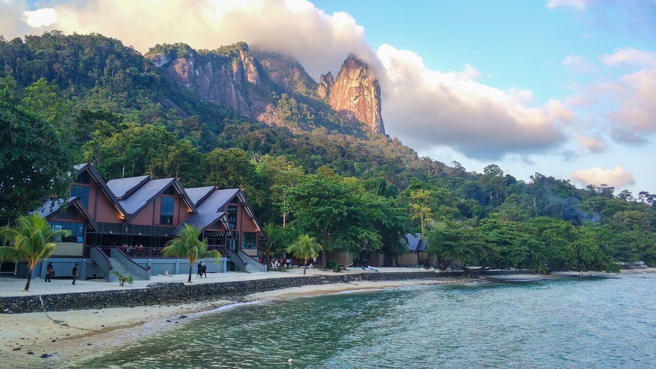 Un hotel costero con varias edificaciones, una playa y una montaña al fondo.