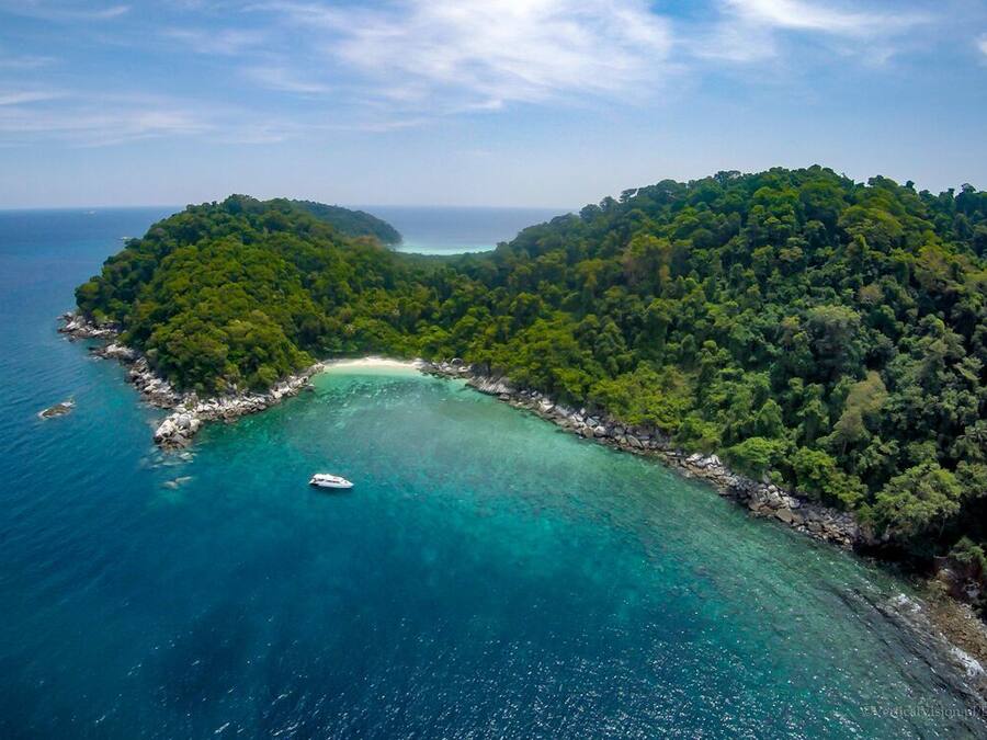 An aerial view of a lush, green island with clear turquoise waters and a small boat.