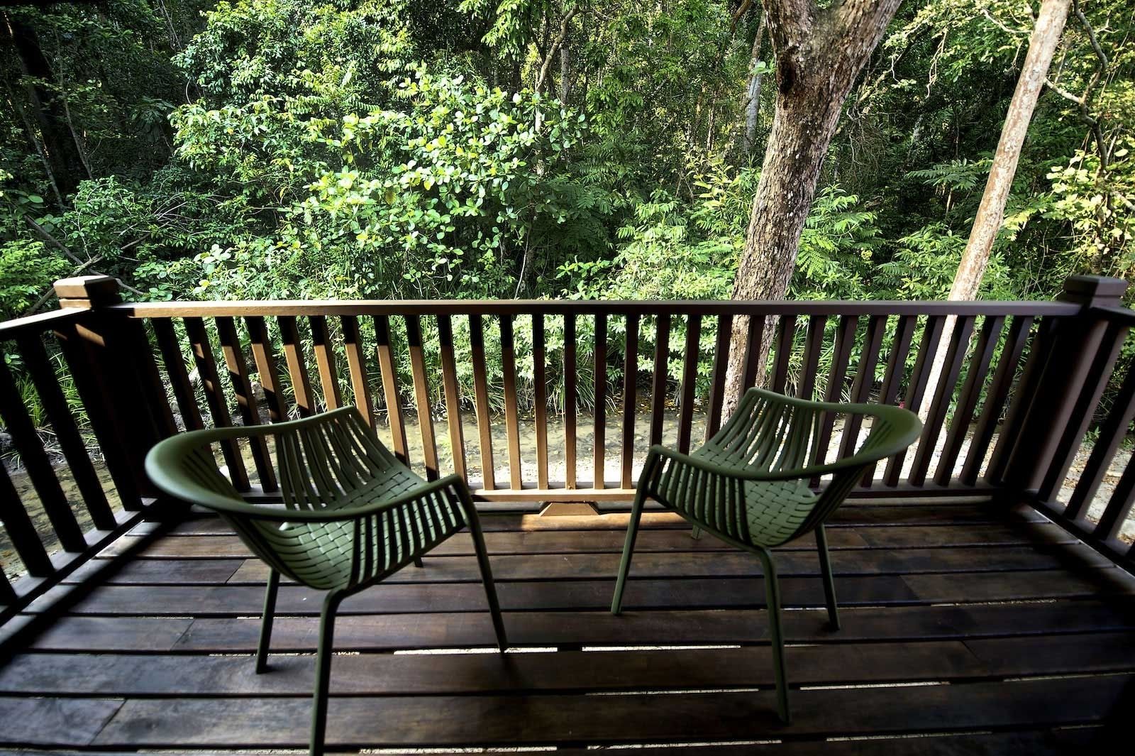Eine Holzterrasse mit zwei grünen Stühlen und einem Holztisch, umgeben von dichtem Wald.