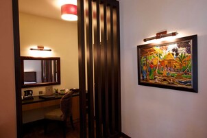 Habitación de hotel con un panel de madera, un escritorio con una computadora portátil, una silla, un espejo y un cuadro en la pared.