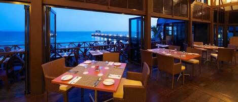 Un restaurante con mesas dispuestas para comer, con vistas a un muelle y al mar.