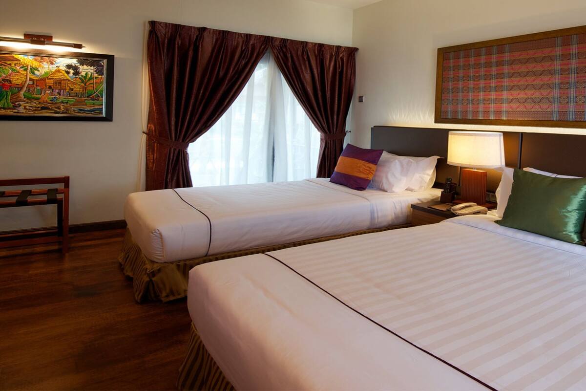 A hotel room with two beds, a nightstand with a lamp, a telephone, and a painting on the wall.