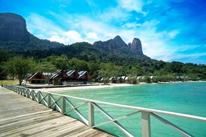 Muelles de madera que conducen a bungalows sobre el agua, con montañas al fondo.