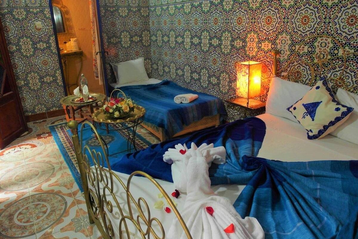 A room with two beds, a nightstand, a lamp, and a decorative mirror.