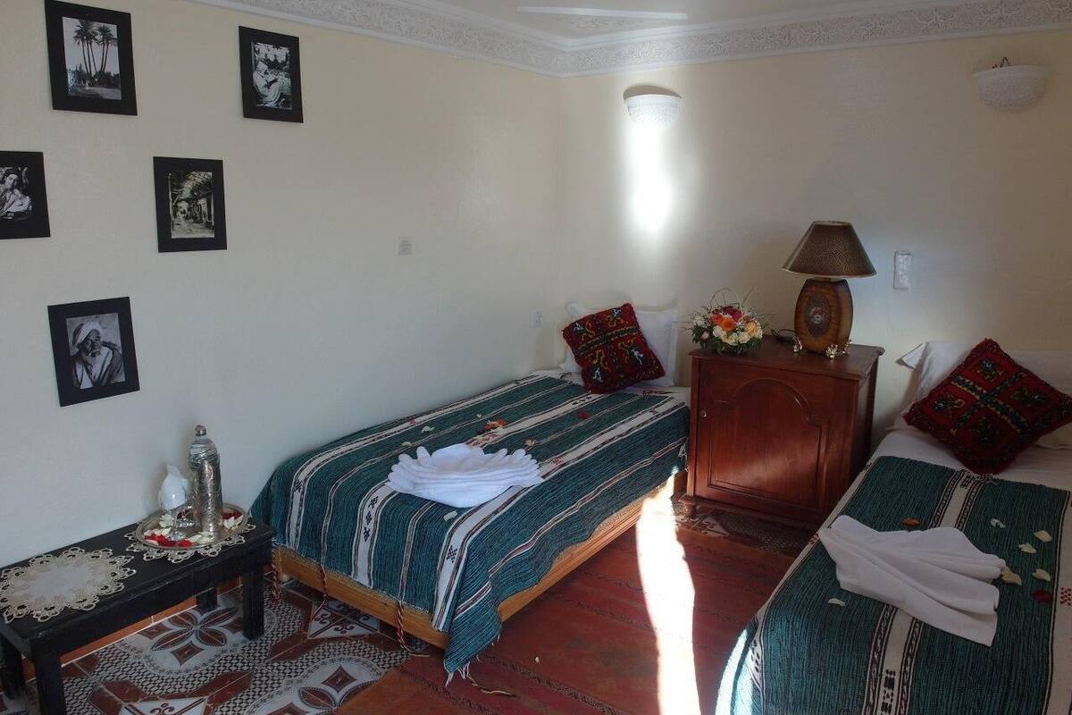 A room with two beds, a wooden cabinet, a table with a decorative item, and framed pictures on the wall.