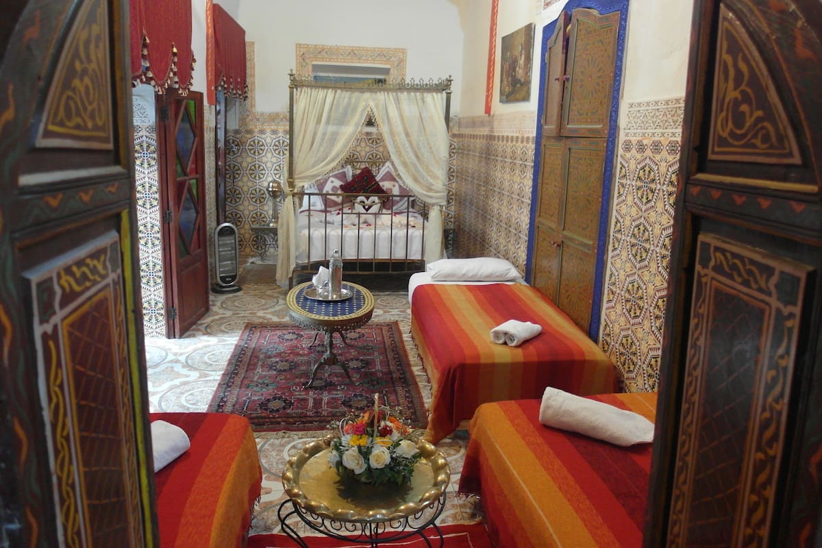A traditional Moroccan room with two beds, ornate doors, and a decorative mirror.