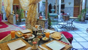 Un coin repas traditionnel marocain, avec une table dressée pour le petit-déjeuner, comprenant du pain, des pâtisseries et des boissons.
