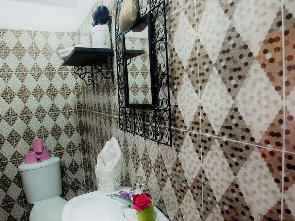 A bathroom with patterned tiles, a toilet, a sink with a mirror, and a shelf with toiletries.
