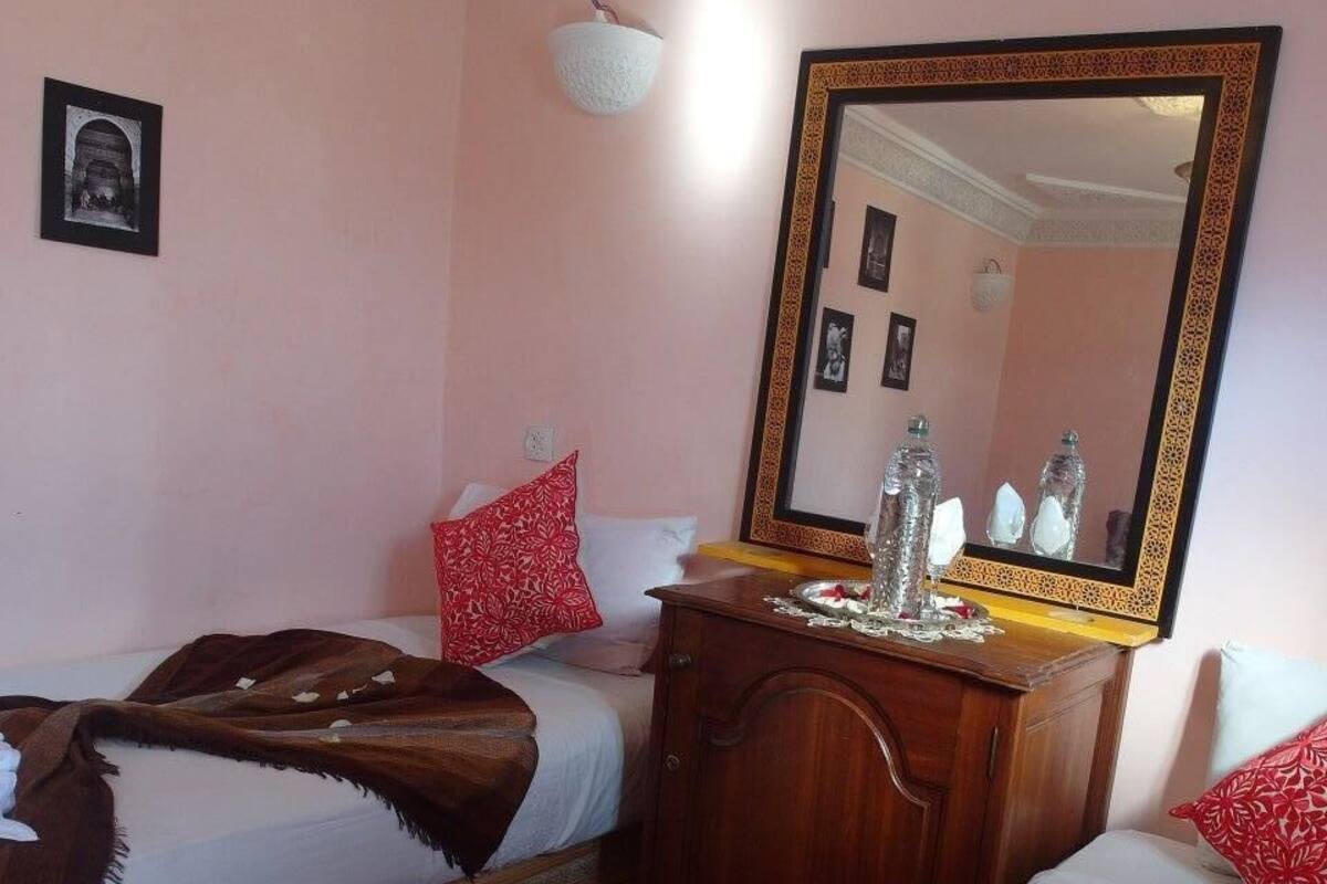 A hotel room with two single beds, a wooden dresser, a mirror, and a red patterned rug.