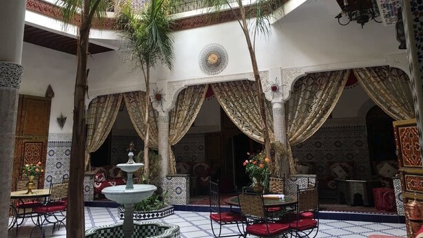 Une cour agrémentée d’une fontaine, de palmiers et d’une décoration marocaine traditionnelle.