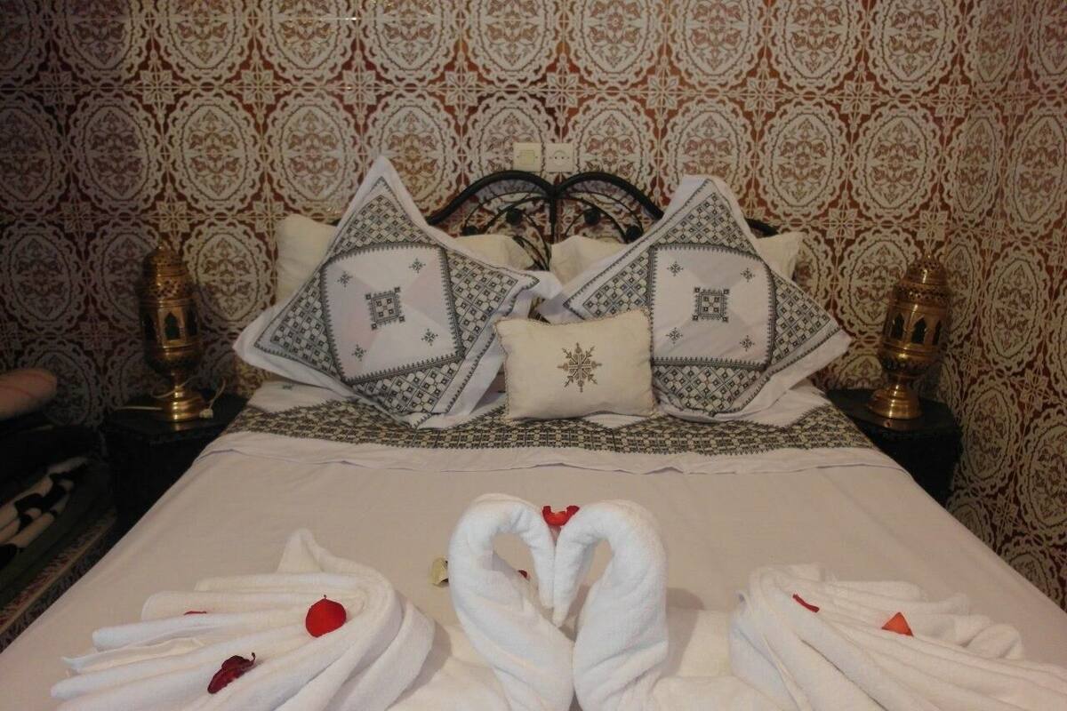 A neatly made bed with a heart-shaped towel arrangement and a decorative pillow.