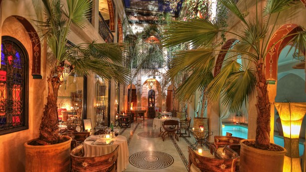 A luxurious interior with ornate chandeliers, potted palm trees, and elegantly set dining tables.