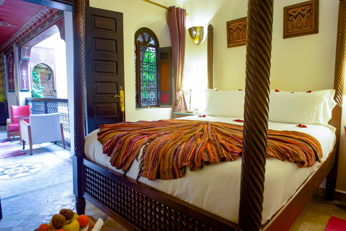 A four-poster bed with a striped bedspread, a wooden headboard, and a window with a view of greenery.