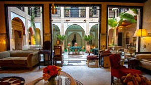 A spacious living area with a central table, sofas, and a view of an outdoor courtyard with arches and plants.