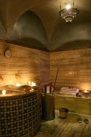 A spa room with a stone wall, a large bathtub, a wooden bench, and a chandelier.