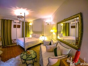 A hotel room with two beds, a sitting area with a glass table, and a large mirror.