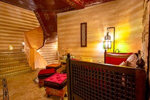 A traditional Moroccan interior with a striped ceiling, a patterned wall, a hanging lantern, and a cushioned bench.
