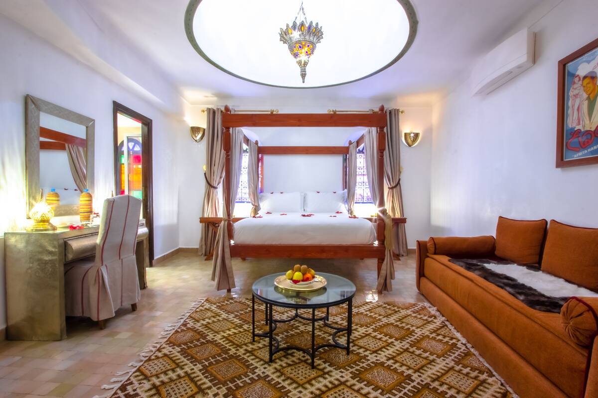 A room with a bed, a sofa, a desk, and a chandelier.