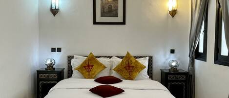 A neatly made bed with a white and yellow bedspread, two decorative pillows, and a framed picture on the wall.