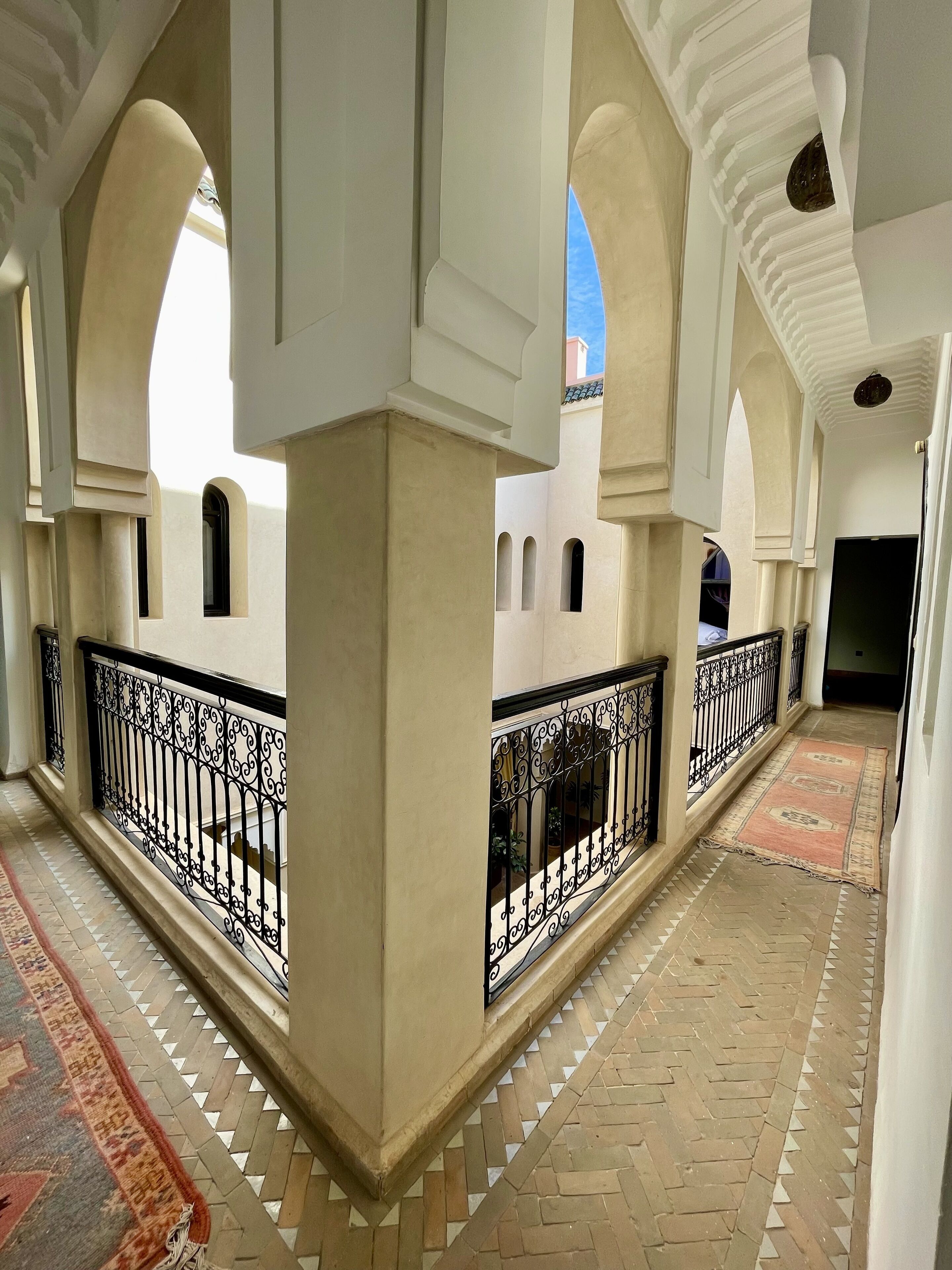 A corridor with arches, a patterned floor, and a railing.