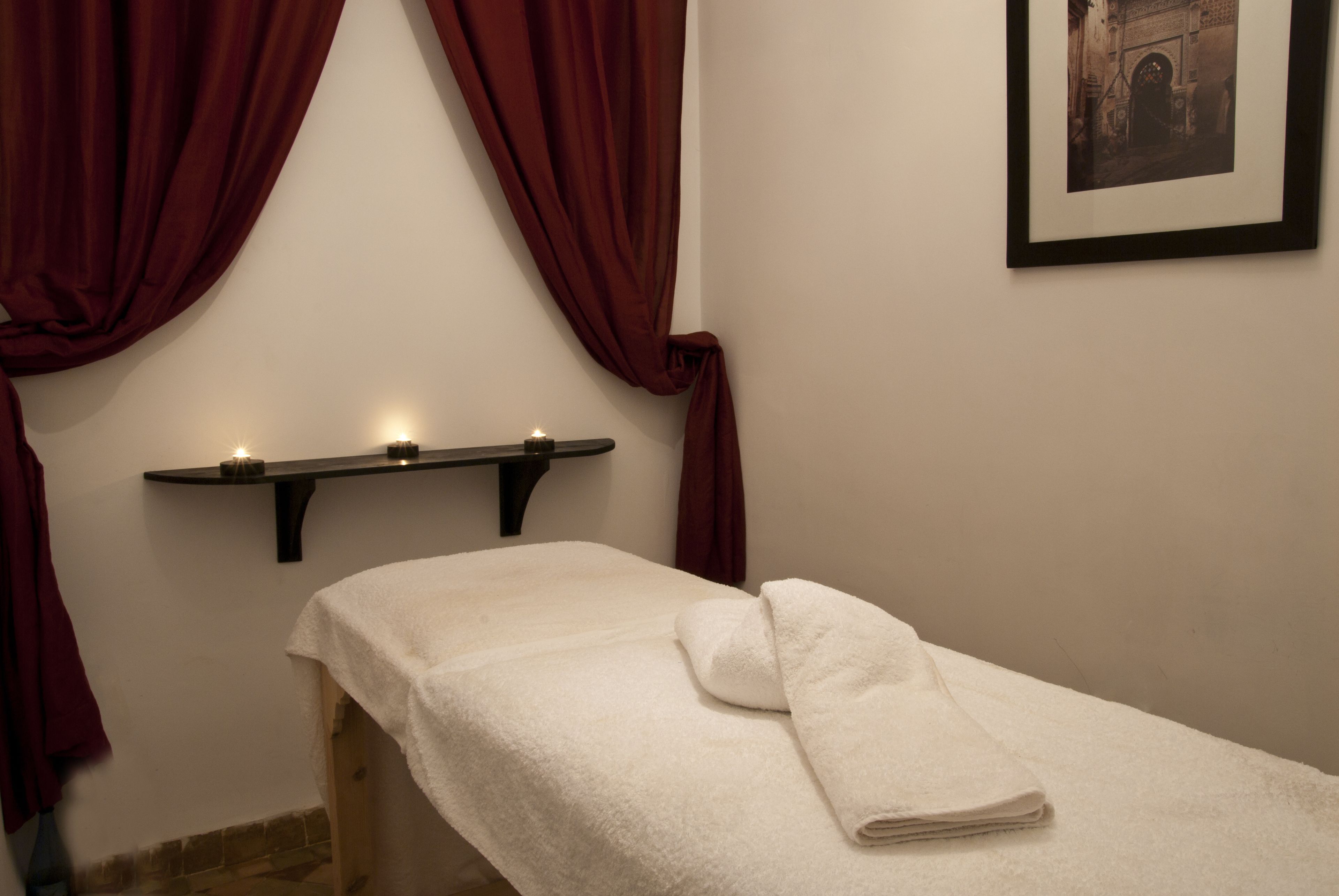 A room with a bed, a shelf with candles, and a framed picture on the wall.