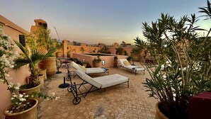 A rooftop terrace with lounge chairs, potted plants, and a view of the cityscape. - Riad Dar Foundouk & Spa (Marrakech)