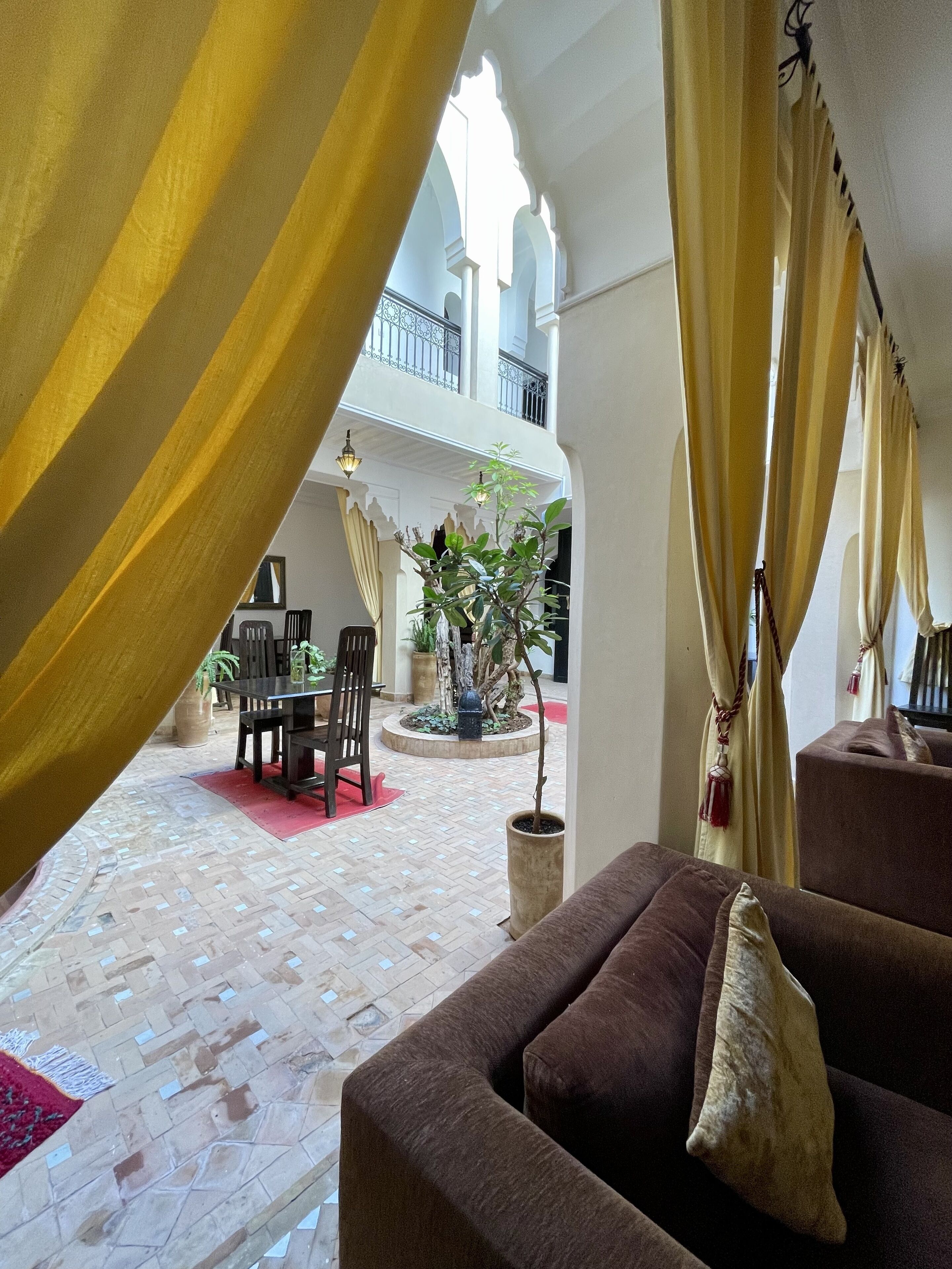 A cozy indoor seating area with a sofa and chairs, a small fountain, and a balcony with a railing.