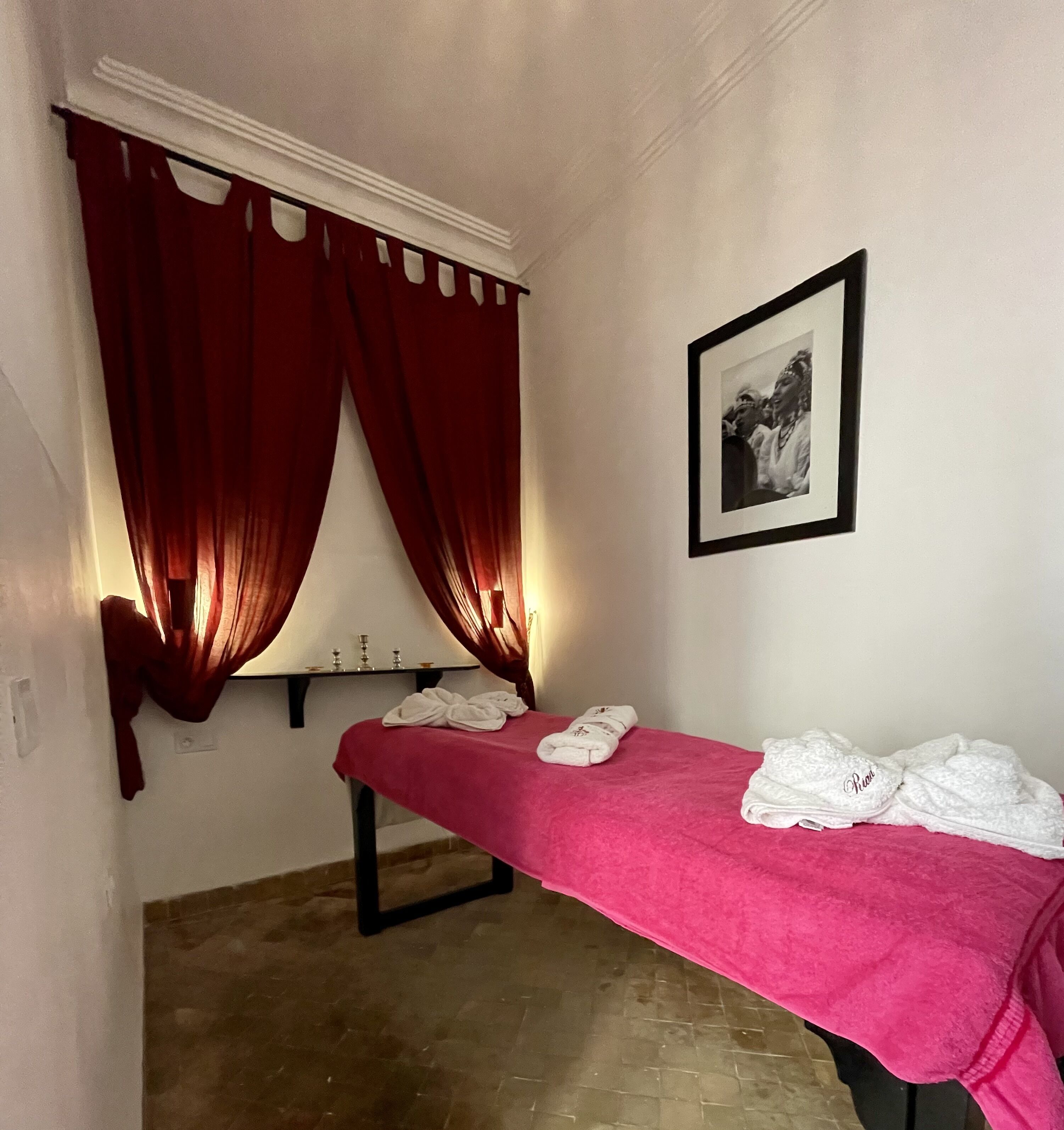 A room with a bed covered in a pink blanket, a framed picture on the wall, and red curtains.