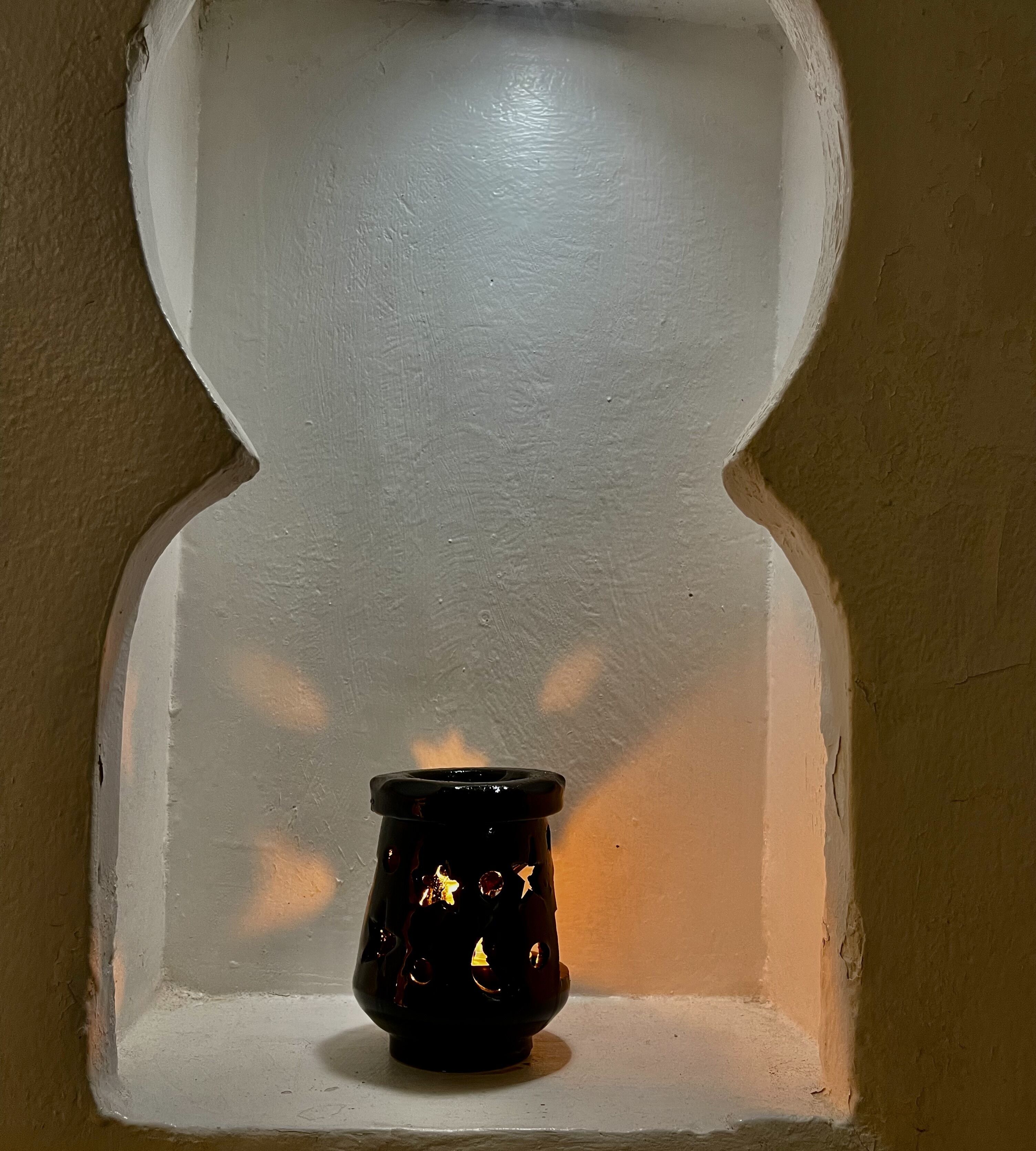 A candle in a white, arched window frame.