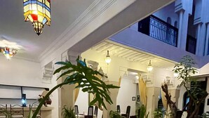 An indoor pool area with a fountain, surrounded by potted plants and a dining area with chairs and tables. - Riad Dar Foundouk & Spa (Marrakech)