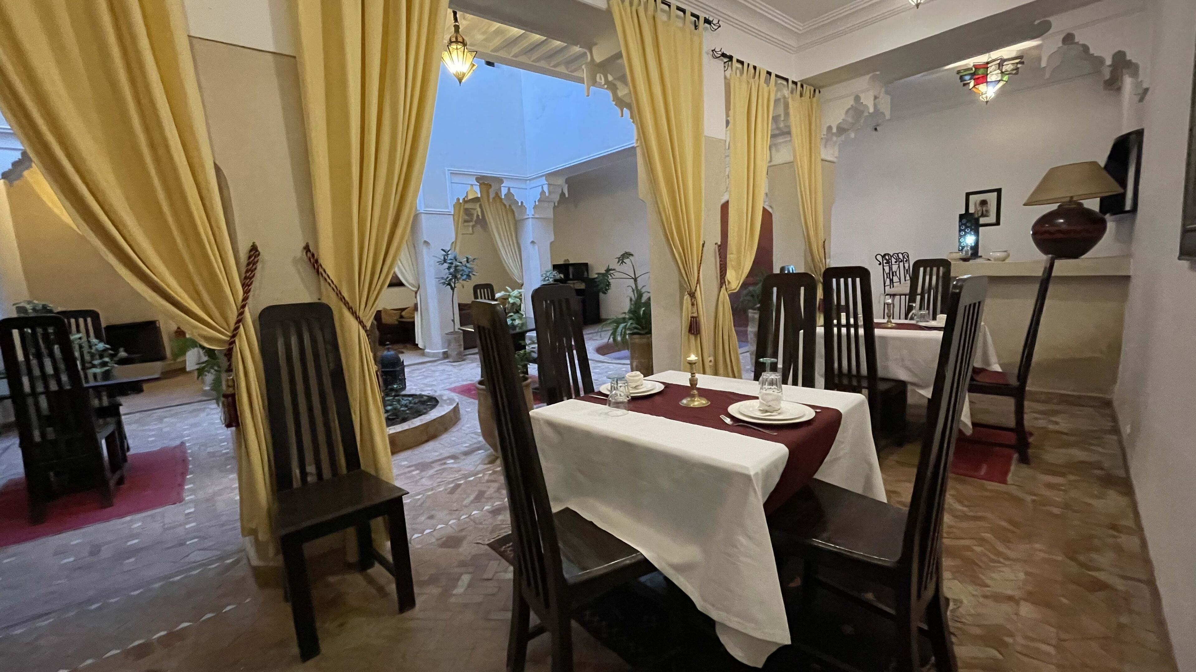 A dining area with tables set for two, chairs, and a chandelier.