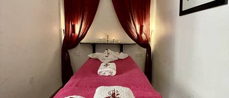 Una habitación de hotel con una cama, cortinas rojas y un cuadro enmarcado en la pared.