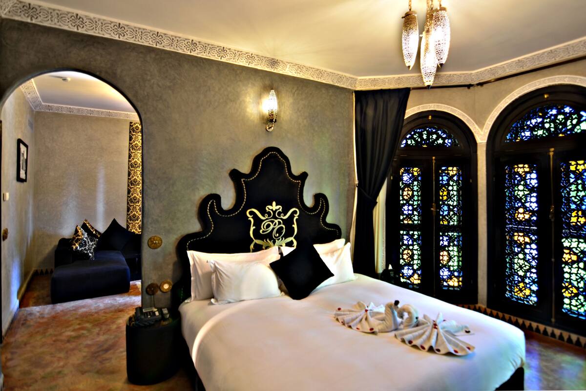 A luxurious hotel room with a large bed, ornate headboard, and stained glass windows.
