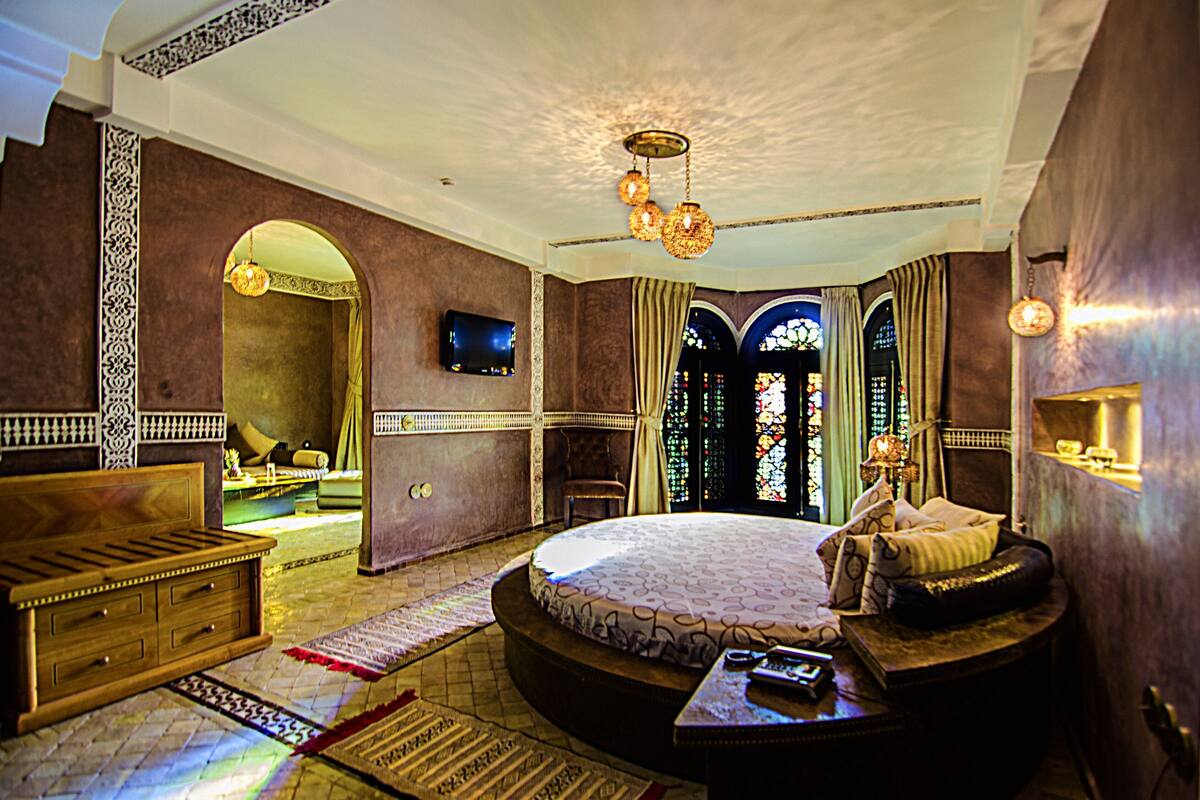 A luxurious bedroom with a large bed, a wooden dresser, a television, and a stained glass window.