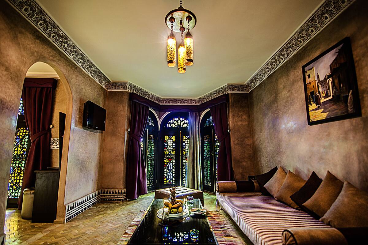 A room with a sofa, a coffee table with fruits, a TV, and a chandelier.