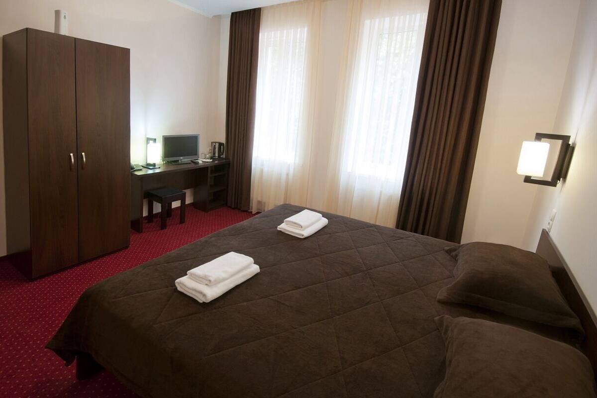 Ein Hotelzimmer mit einem großen Bett, einem Schreibtisch mit Computer, einem Kleiderschrank und Vorhängen.