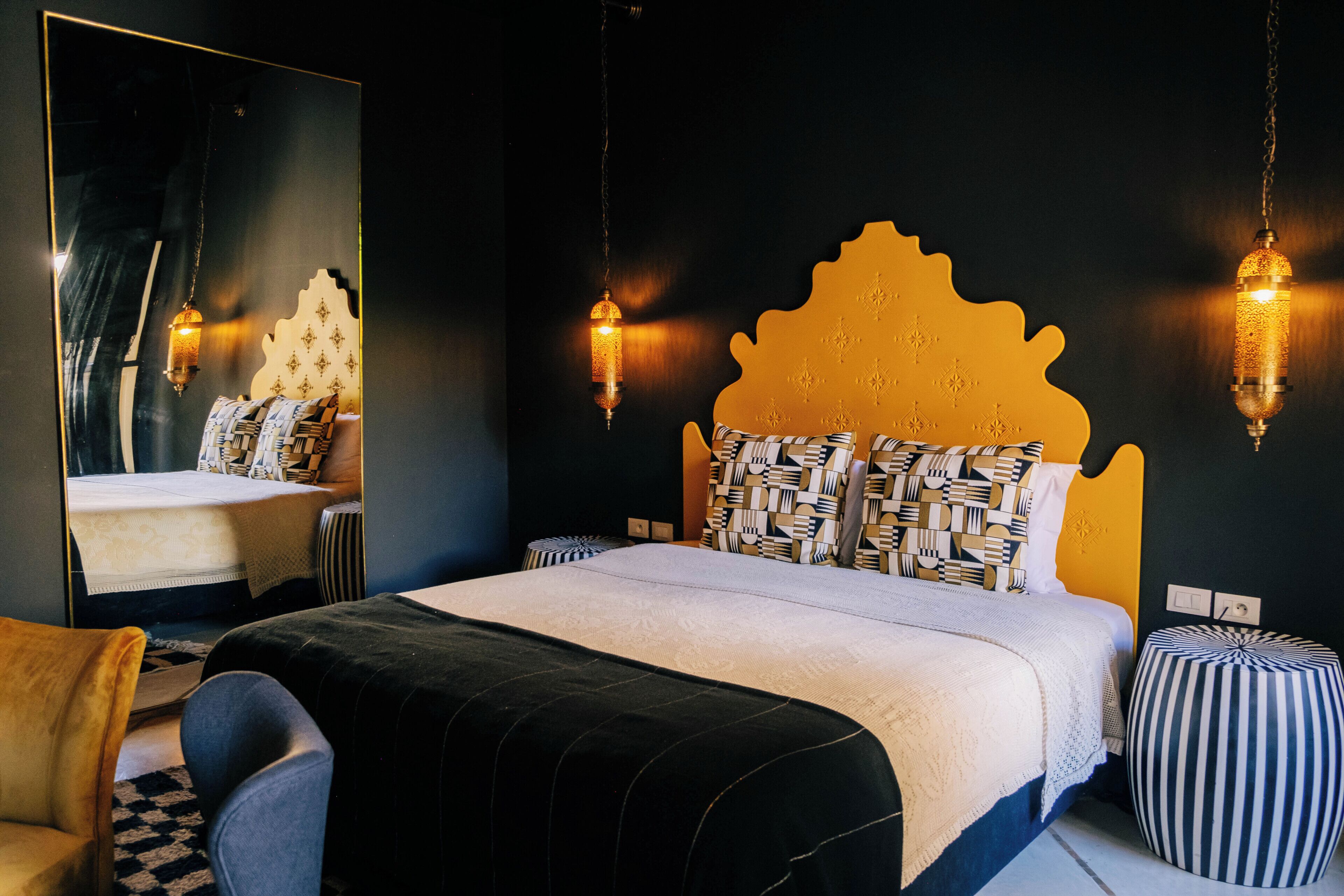 A bedroom with a large bed, a mirror, hanging lamps, and striped ottomans.