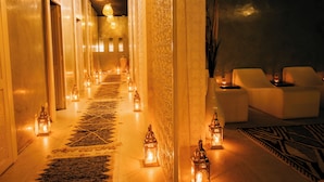 A corridor with a patterned carpet, wall-mounted lanterns, and white lounge chairs. - Riad Nashira & Spa (Marrakech)