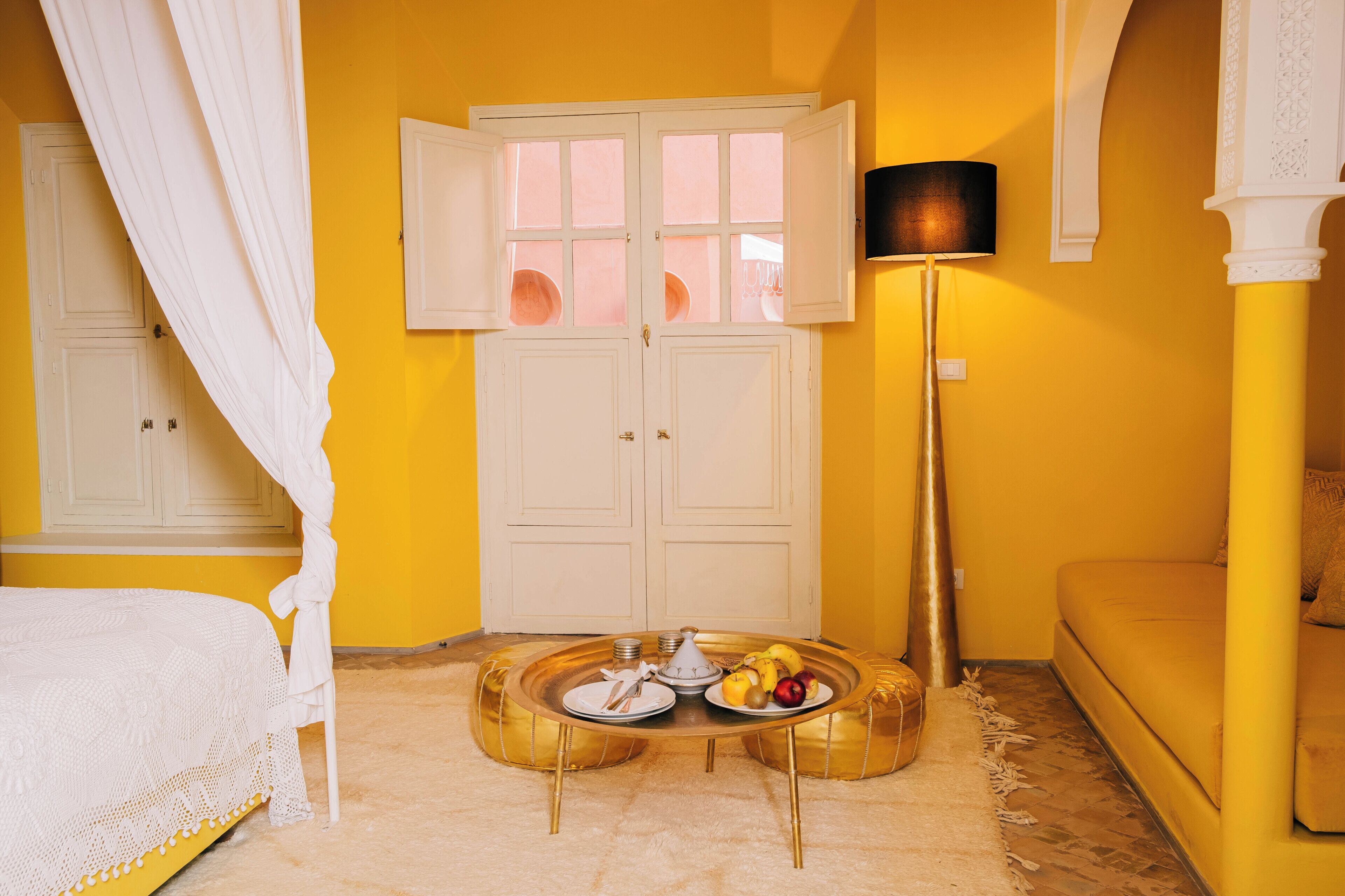 Una habitación con una cama, una mesa de comedor con platos y frutas, una lámpara y un sofá.