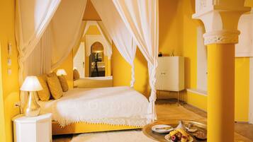 Una habitación con una cama, una mesita de noche, una mesa con fruta y un espejo decorativo.