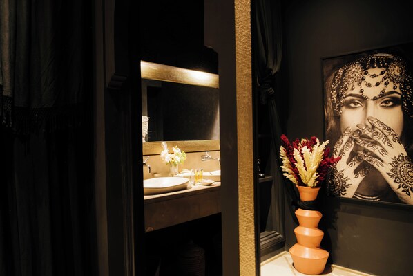 A bathroom with a mirror, sink, and a decorative vase with flowers.