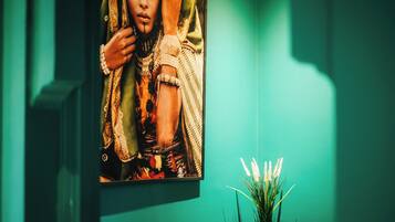 Une œuvre d’art encadrée sur un mur de couleur turquoise, un petit vase noir avec des fleurs blanches et un objet rectangulaire noir.
