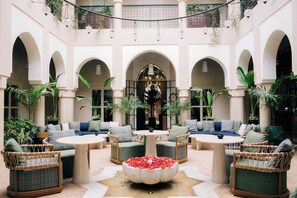 A spacious courtyard with multiple seating areas, including sofas and chairs, surrounded by potted plants and a central decorative fountain. - Riad Nashira & Spa (Marrakech)