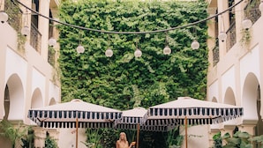 A pool area with striped lounge chairs and umbrellas, surrounded by greenery and architectural arches. - Riad Nashira & Spa (Marrakech)
