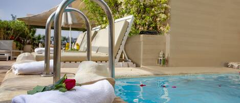 A poolside area with lounge chairs, a metal pool ladder, and a white towel with a rose.